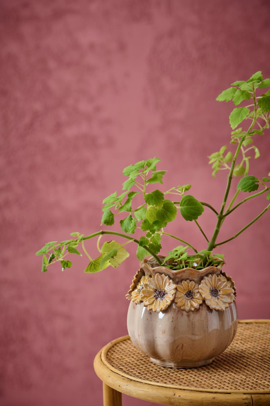 Solsikkevase fra Ib Laursen med grønne grene på flettet sidebord foran rosa væg i hyggelig boligindretning.