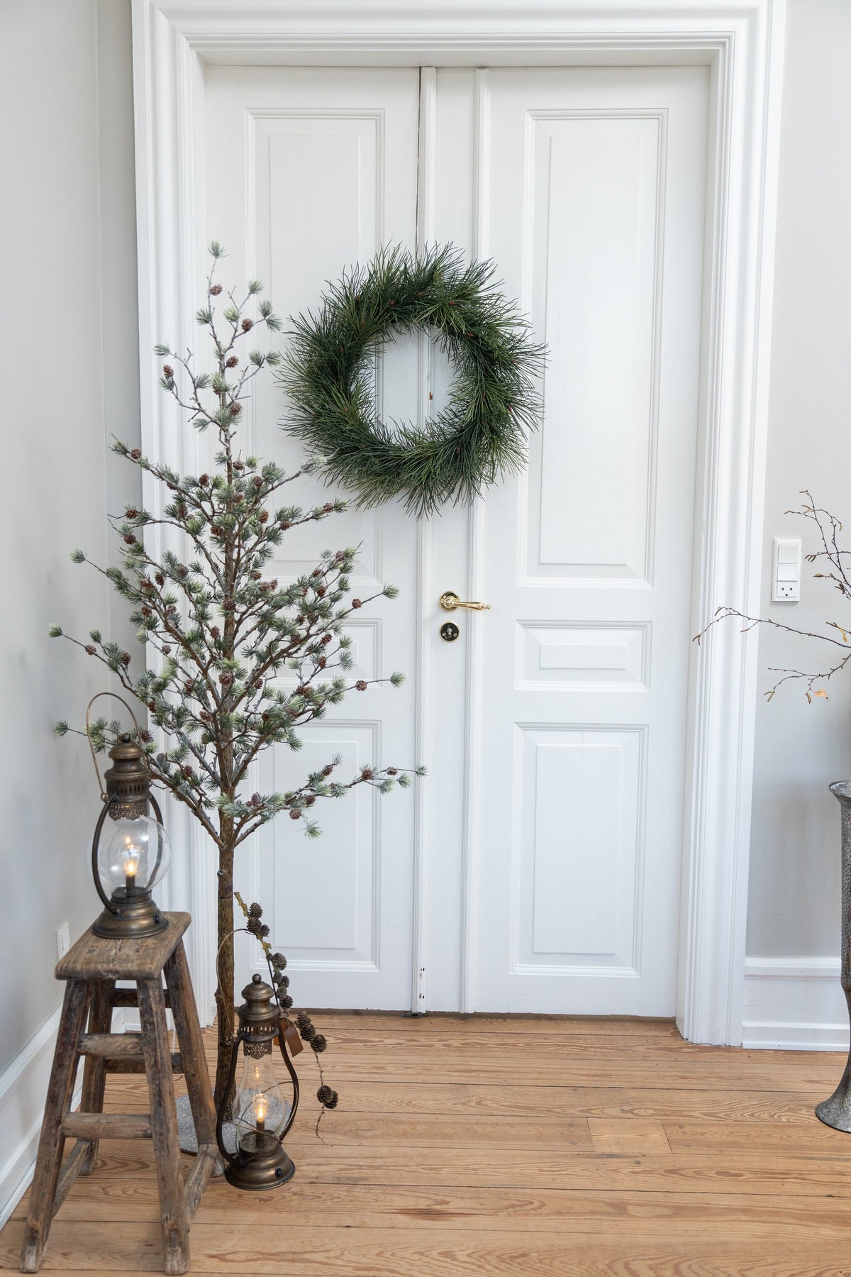 Nostalgisk LED stormlygte i antik bronze placeret ved en træskammel og dekorative grene i en lys entré med julepynt.