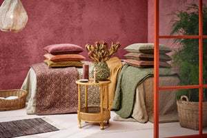 Foldede quilts og puder fra Ib Laursen i forskellige farver og mønstre ved en rosa væg