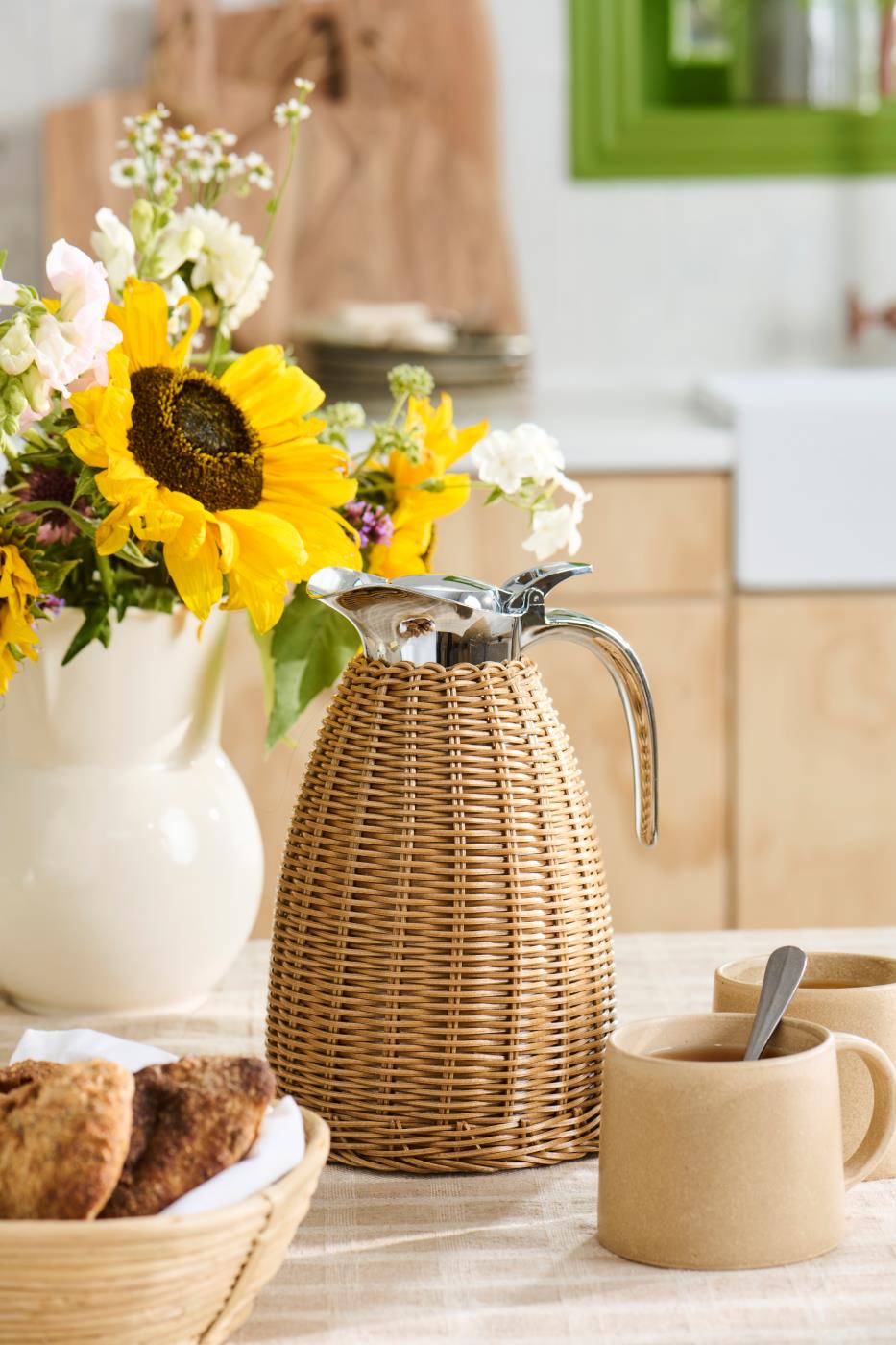 Termokande i brun polyrattan på dækket kaffebord med solsikker, keramik og friskbagt brød.