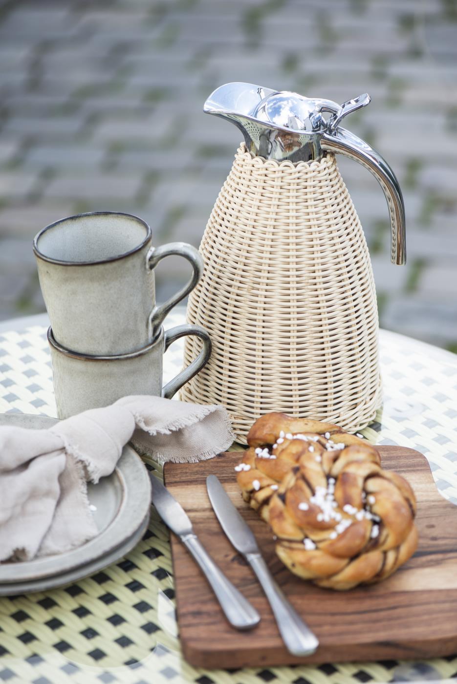 Flettet termokande fra Ib Laursen på udendørs kaffebord med keramikkrus, croissant og rustikt service.