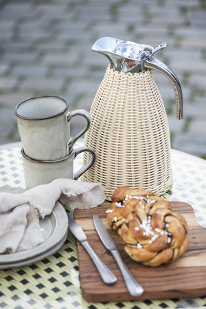 Flettet termokande fra Ib Laursen på udendørs kaffebord med keramikkrus, croissant og rustikt service.