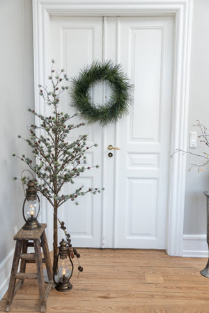 Nostalgisk LED stormlygte i antik bronze placeret ved en træskammel og dekorative grene i en lys entré med julepynt.