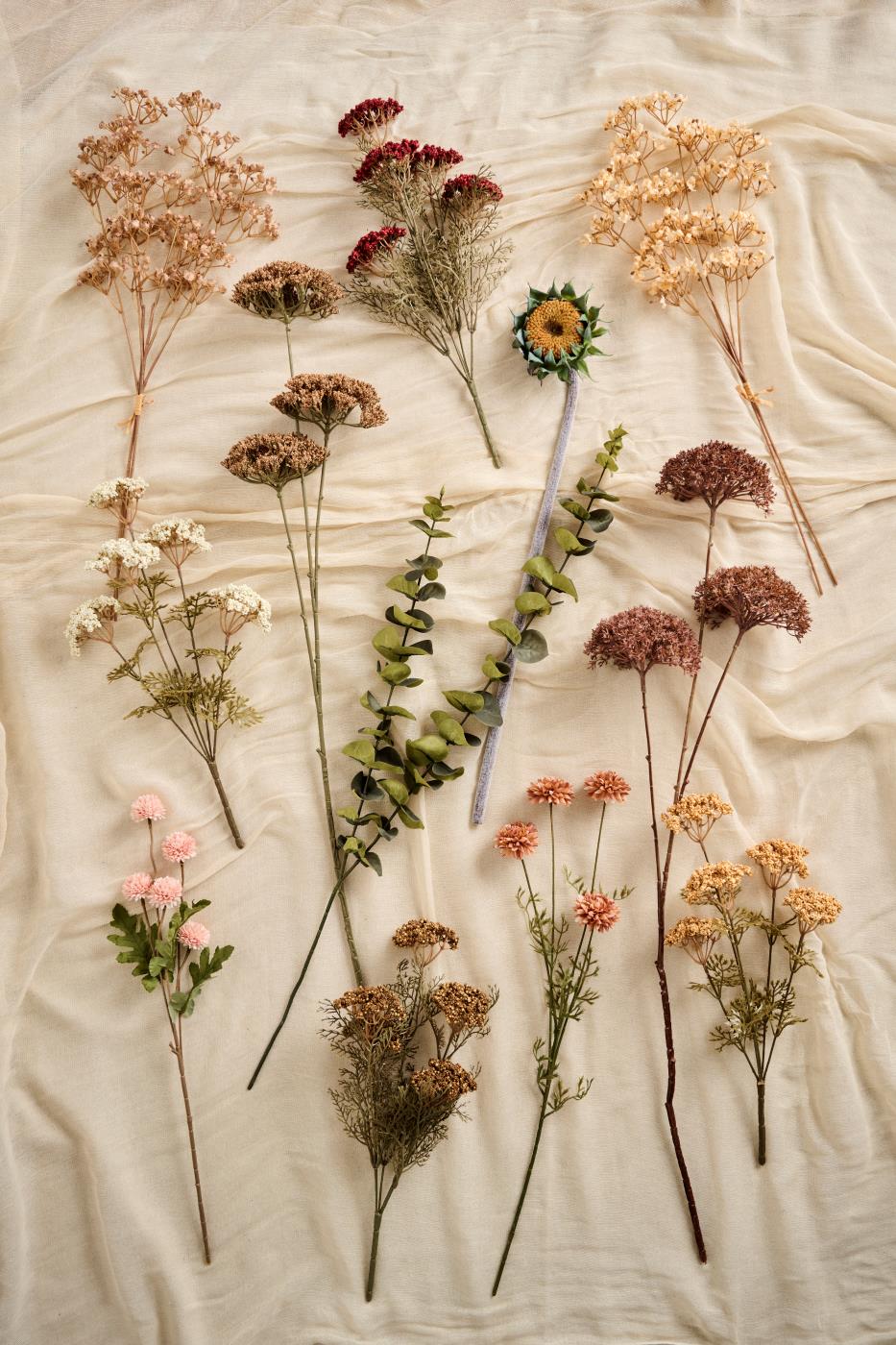 Kunstige efterårsblomster fra Ib Laursen i varme brune, gyldne og rosa nuancer arrangeret på lyst stof.