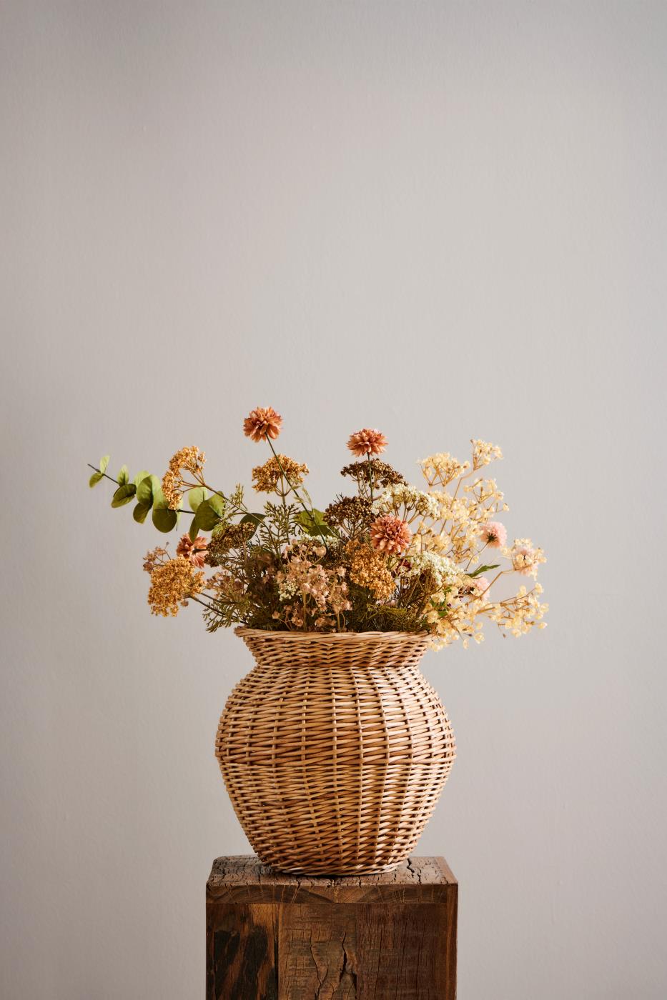 Efterårsbuket med kunstig eukalyptus og blomster i gyldne, brune og cremefarvede nuancer i flettet vase.