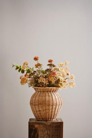 Efterårsbuket med kunstige blomster i hvide, orange og gyldne nuancer i rustik flettet vase.