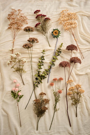Kunstige efterårsblomster fra Ib Laursen i brune, cremefarvede og rosa nuancer arrangeret på lyst stof.