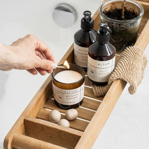 En hånd tænder et Ib Laursen ALTUM Meadow duftlys i brunt glas på bakke over badekar