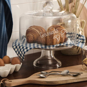 Kagefad i glas på fod fra Ib Laursen med croissanter og blåternet dug under glasklokke med ordet croissant skrevet på i hvid skrift